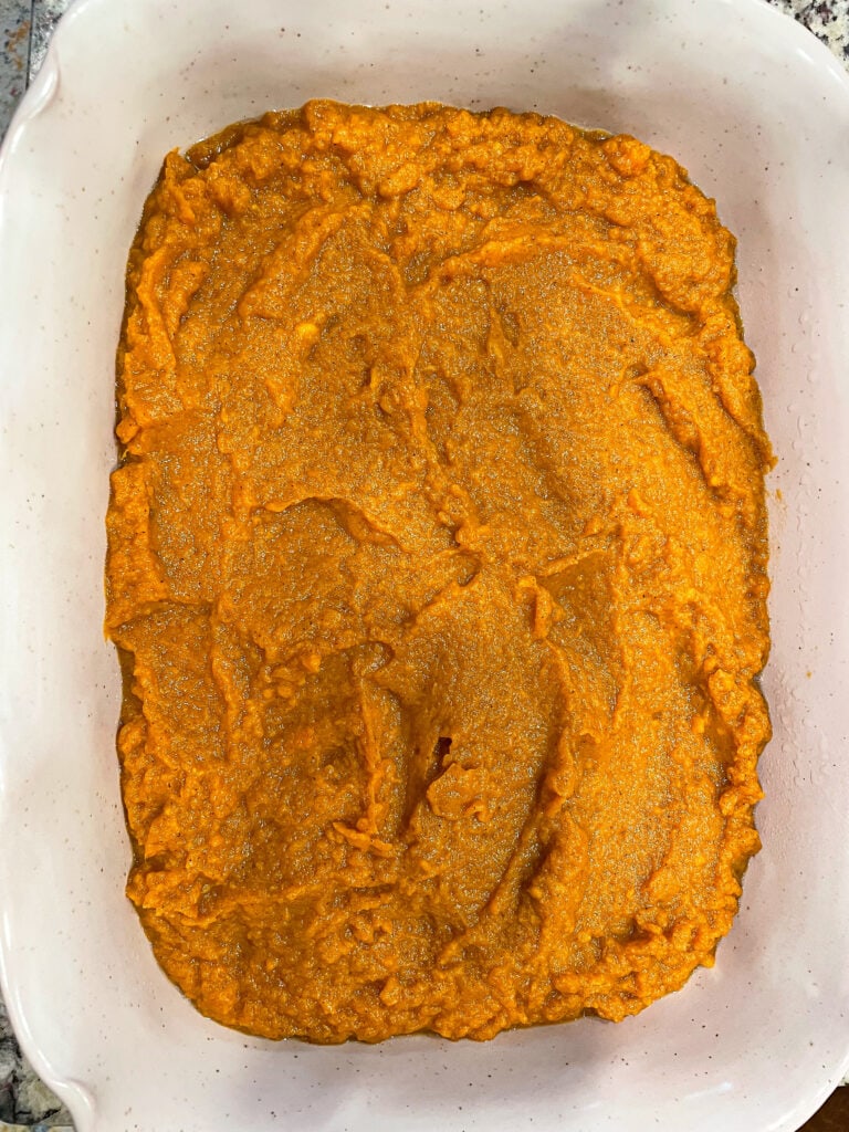 overhead shot of mashed sweet potatoes spread out into a glass baking dish.