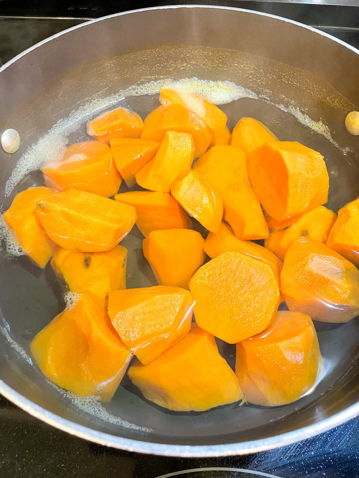 overhead shot of chopped, boiled sweet potatoes in water in a stockpot.
