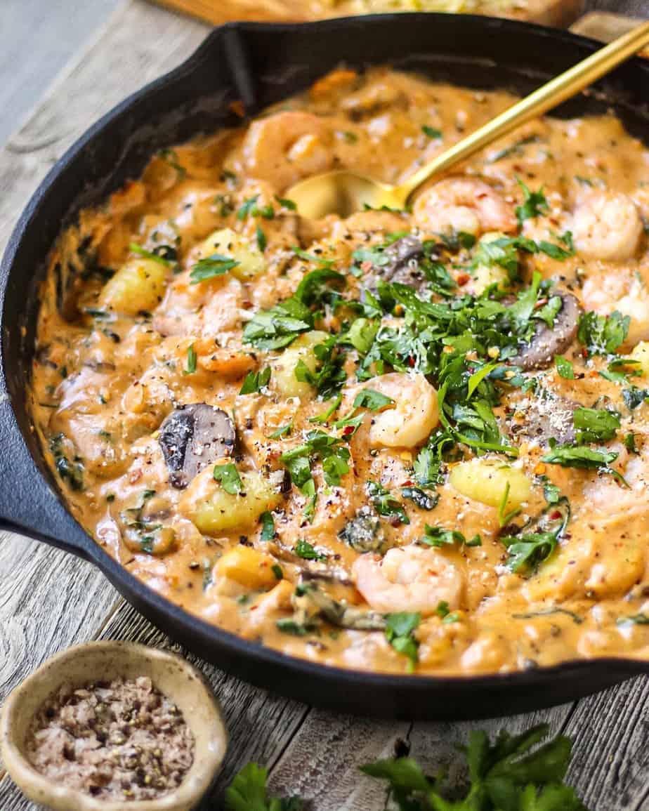 angled shot of Creamy Cajun Shrimp and Gnocchi Skillet in a cast iron skillet on top of white washed wooden surface. striped linen in perimeter.