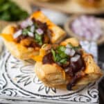 side angle shot of Sweet & spicy bbq chicken puff pastry cups on a gray plate on wooden surface. chopped red onion and cilantro in perimeter of shot