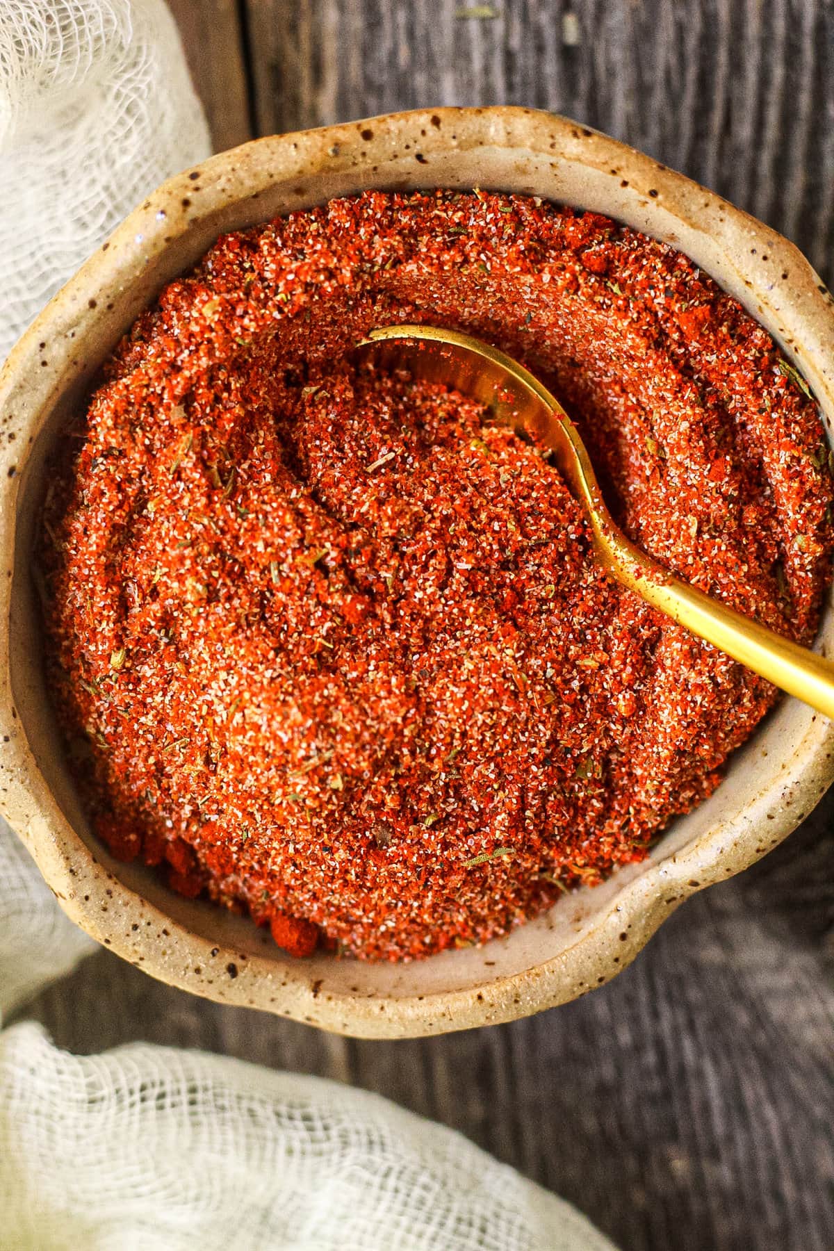 overhead shot of blackening seasoning in a gray bowl on a wooden surface. small gold spoon in the bowl.