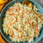 Creamy southern coleslaw in a blue bowl with an orange linen underneath.