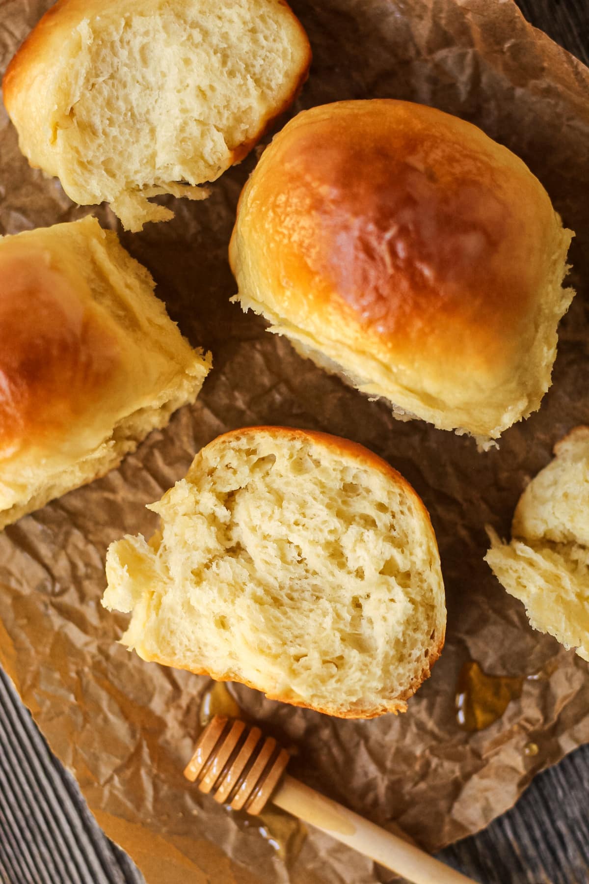 honey butter dinner rolls on parchment paper. One roll torn open to show texture.