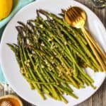 Honey lemon roasted asparagus on a white plate with a gold fork and spoon.