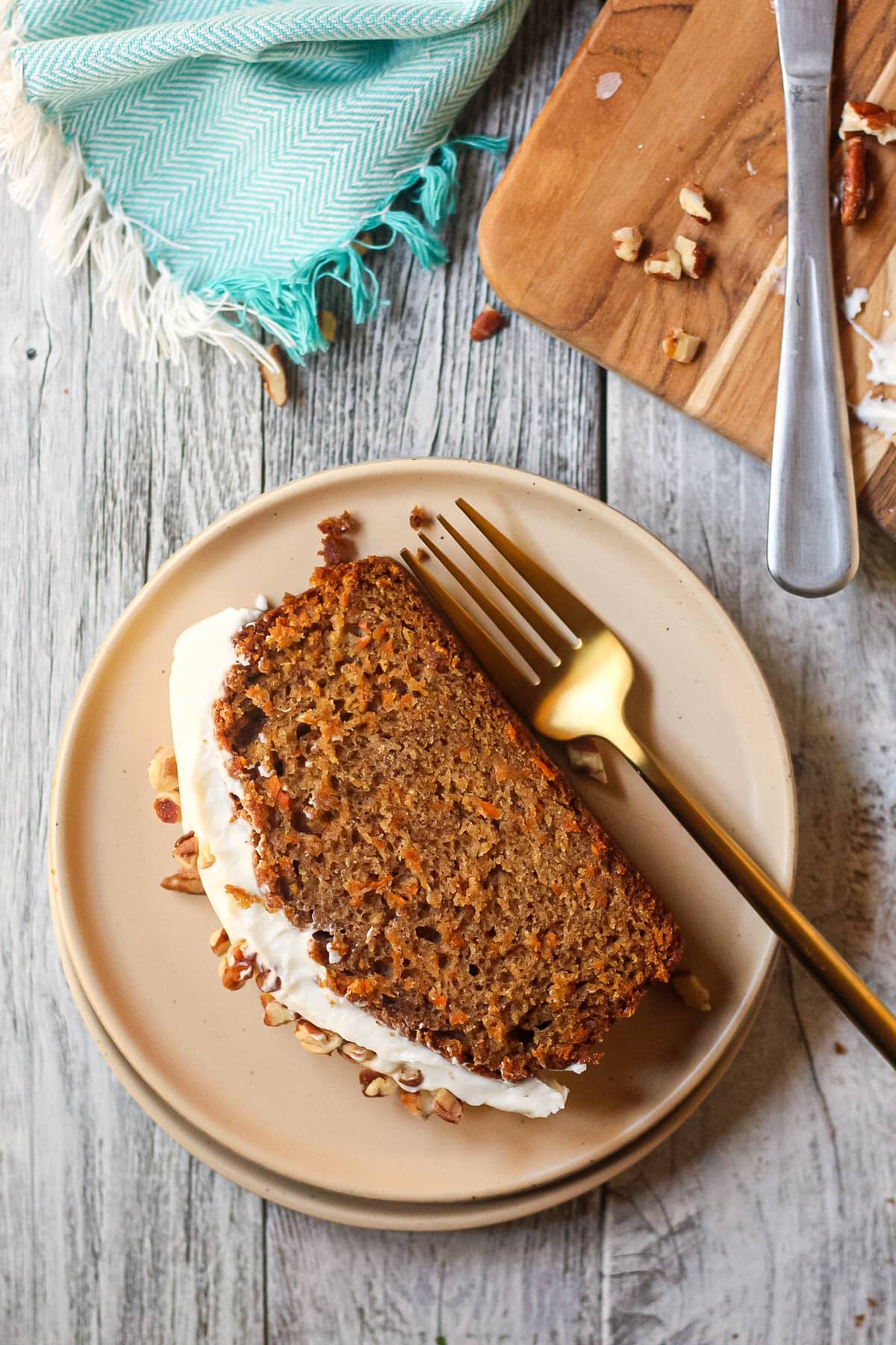 slice of carrot cake loaf with cream cheese frosting on a brown plate