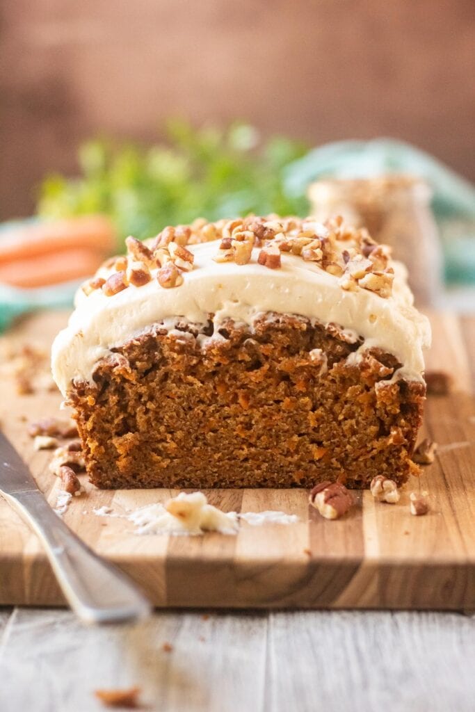 carrot loaf cake with cream cheese frosting on wooden cutting board