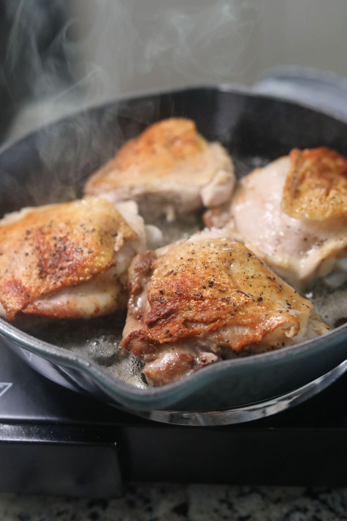 chicken thighs cooking in a skillet.
