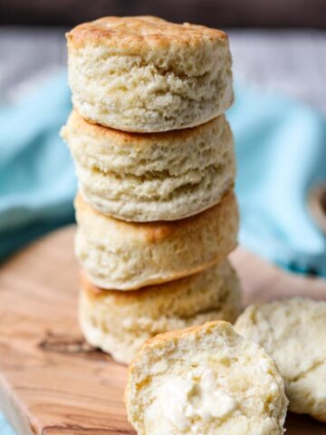 sour cream biscuits stacked on a wooden cutting board.