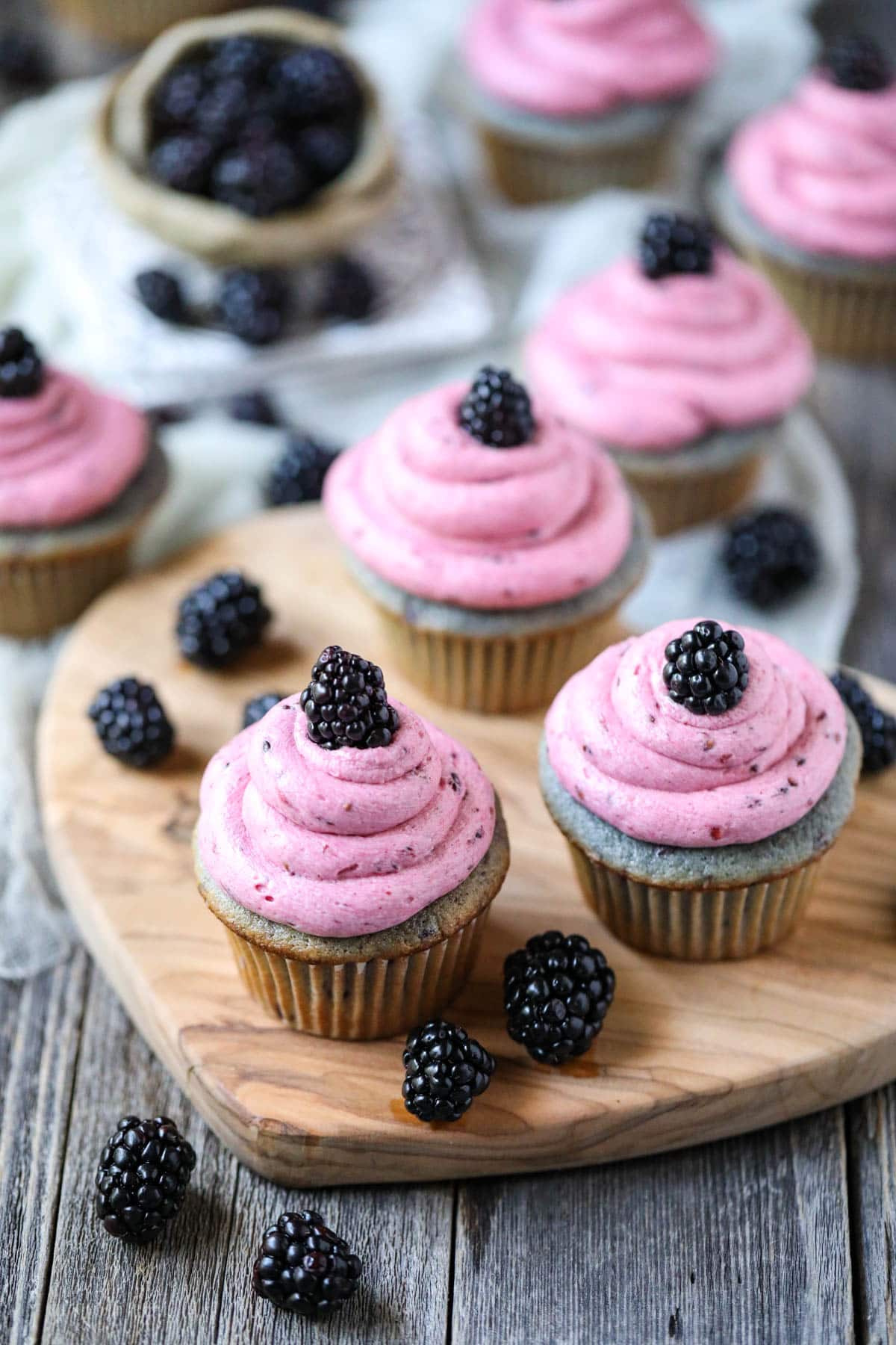 blackberry cupcakes on a wooden cutting board with blackberries and mint leaves scattered around.