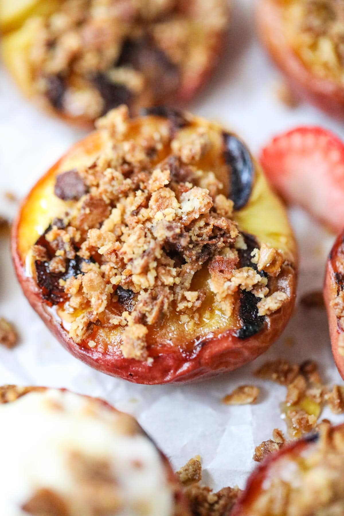 maple grilled peaches with granola topping on white parchment paper.
