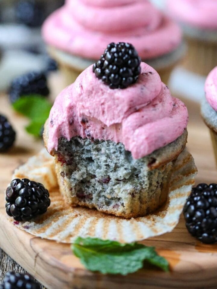 blackberry cupcakes on a wooden cutting board with blackberries scattered around.