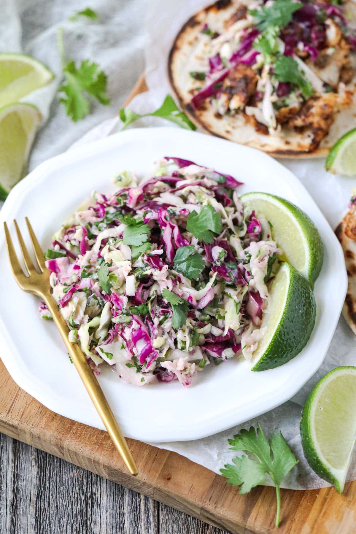 cilantro lime slaw on a white plate with gold fork.