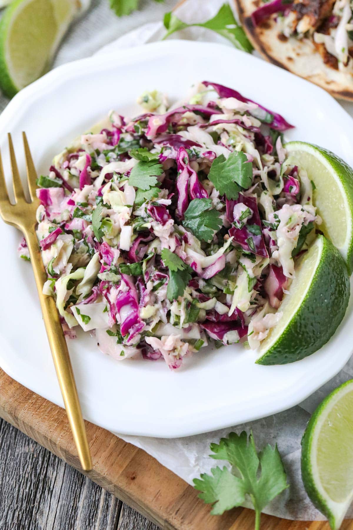 cilantro lime slaw on a white plate with gold fork.