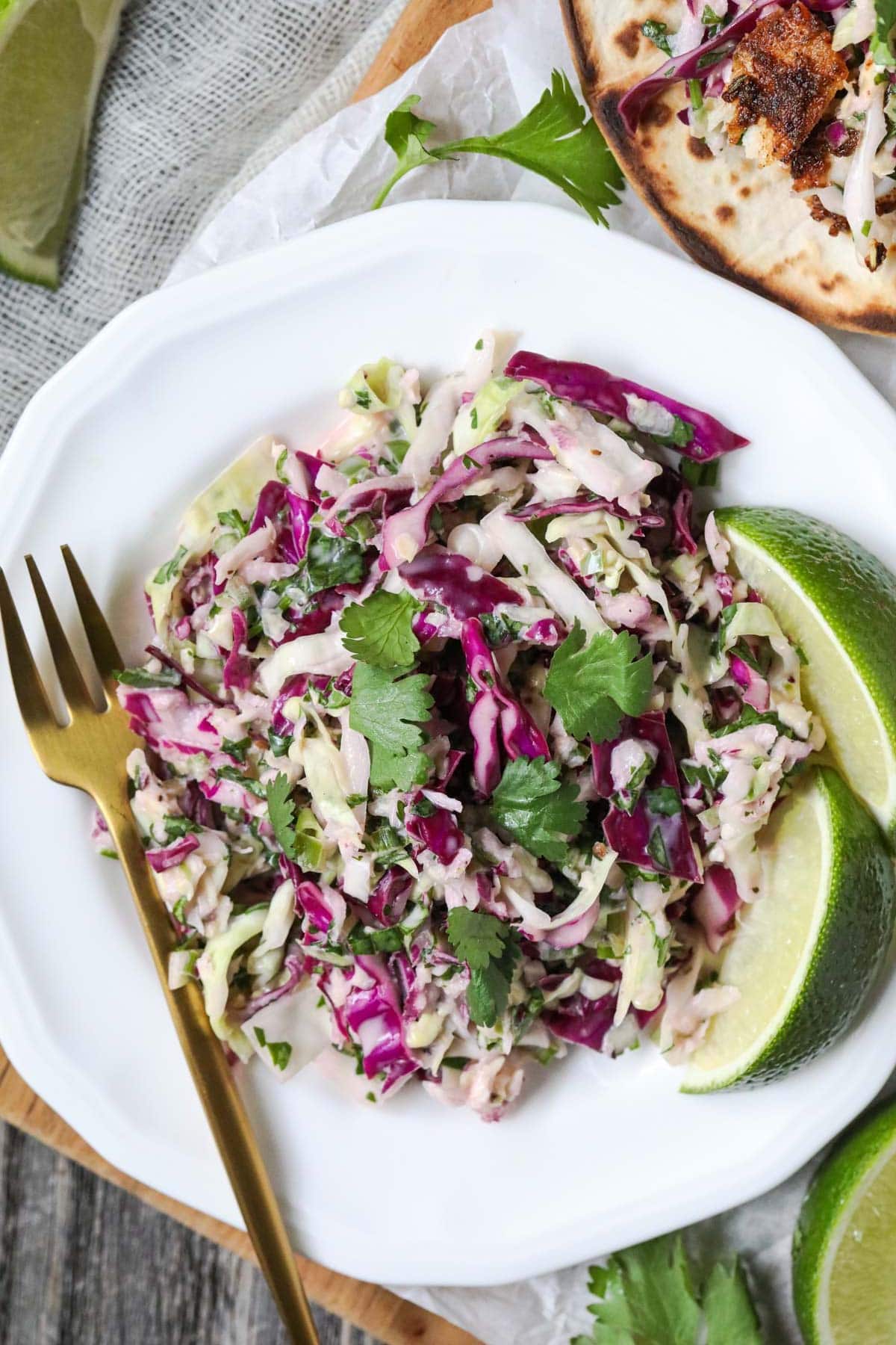 cilantro lime slaw on a white plate with gold fork.