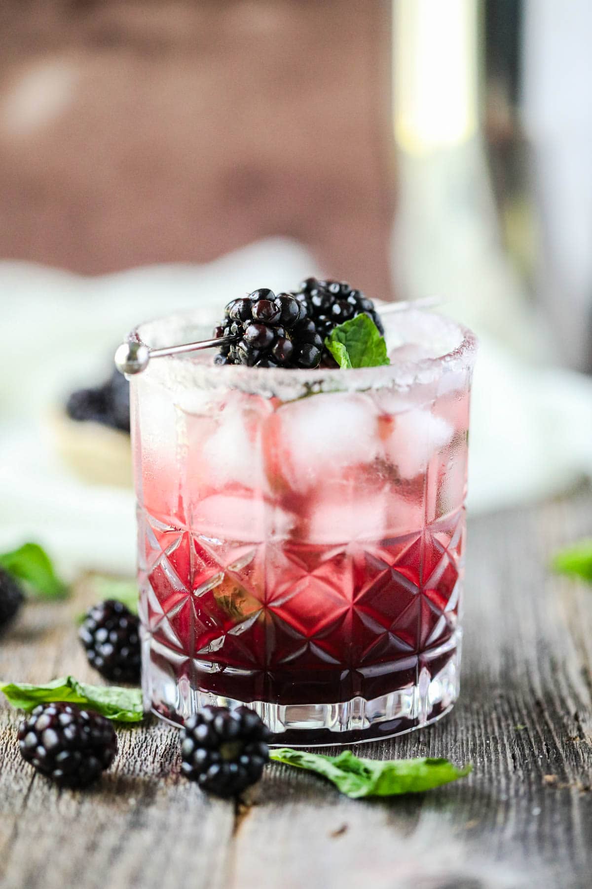 blackberry smash mocktail on a wooden surface with cocktail shaker in the background.