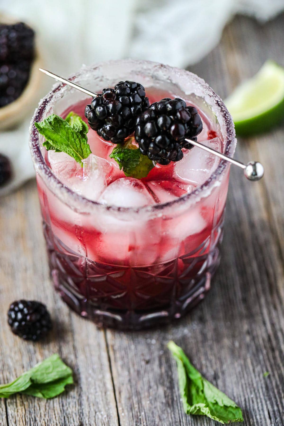 blackberry smash mocktail on a wooden surface with mint leaves and blackberries scattered around.