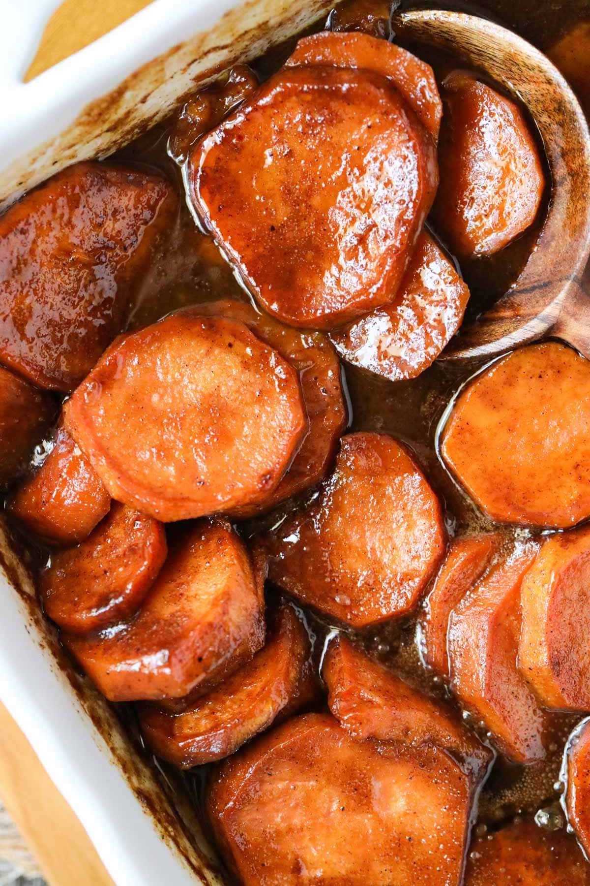 southern candied yams in a white baking dish with a serving spoon in the right corner.
