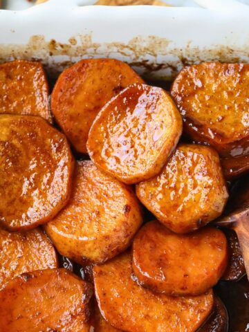 Southern candied yams in a white baking dish with a wooden serving spoon.