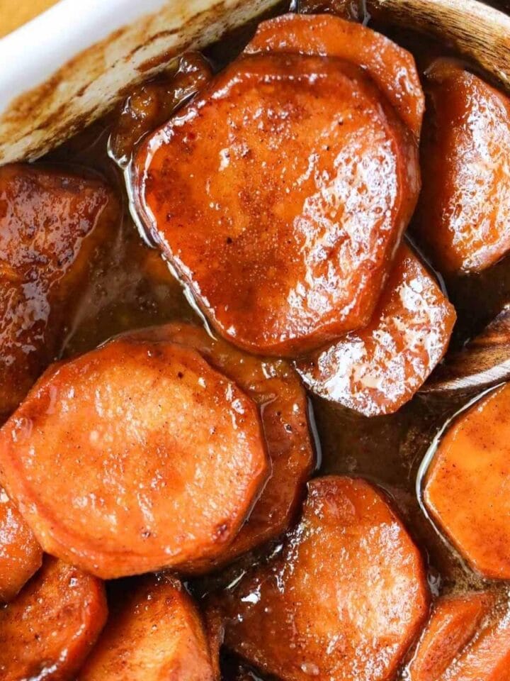 southern candied yams in a white baking dish with a serving spoon in the right corner.