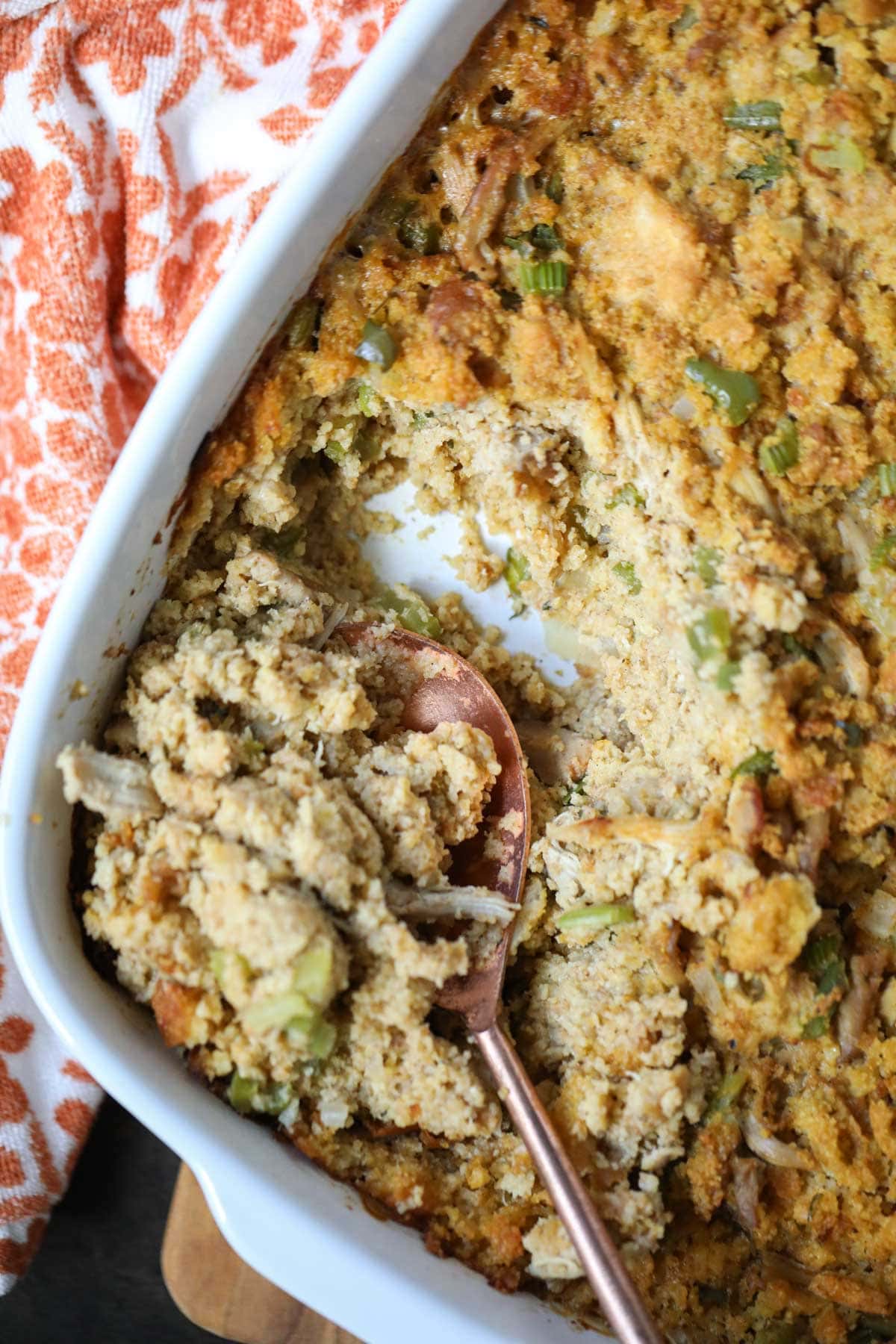 southern cornbread dressing in a white baking dish with a spoon in the pan withan orange and white linen underneath.