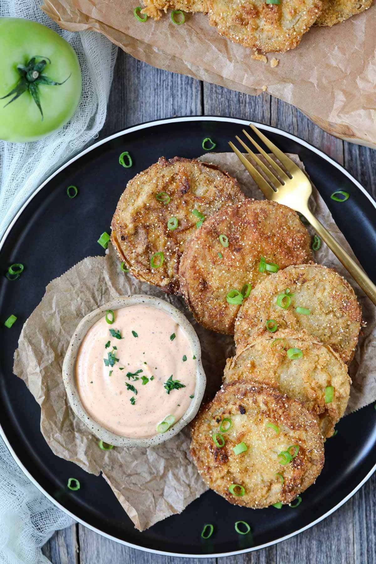 fried green tomatoes on a black plate served with creamy dipping sauce in a cup.