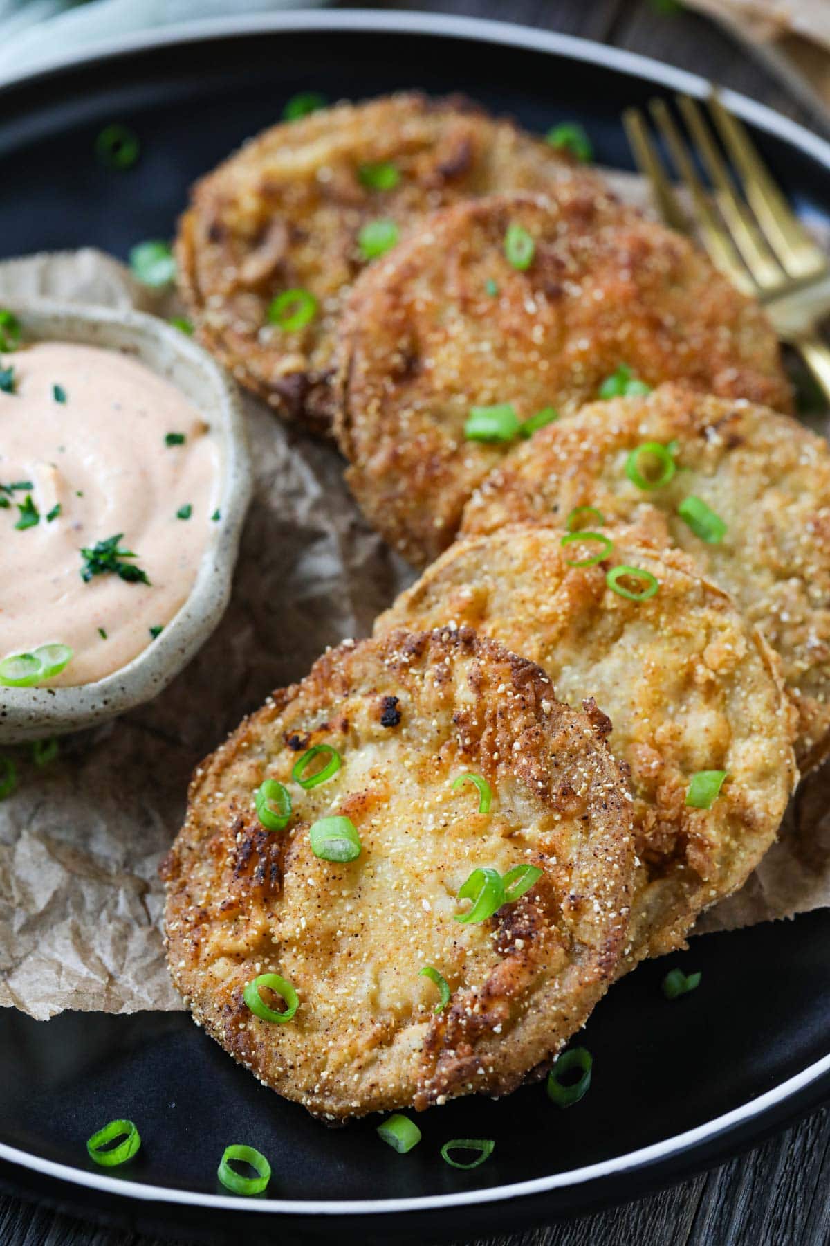 fried green tomatoes on a black plate served with creamy dipping sauce in a cup.