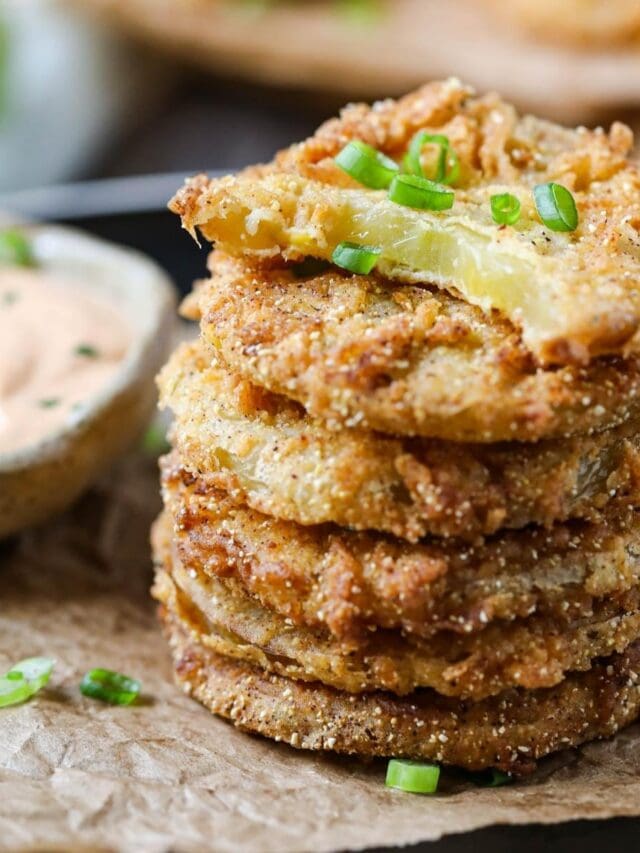 fried green tomatoes stacked on a black plate served with creamy dipping sauce in a cup.