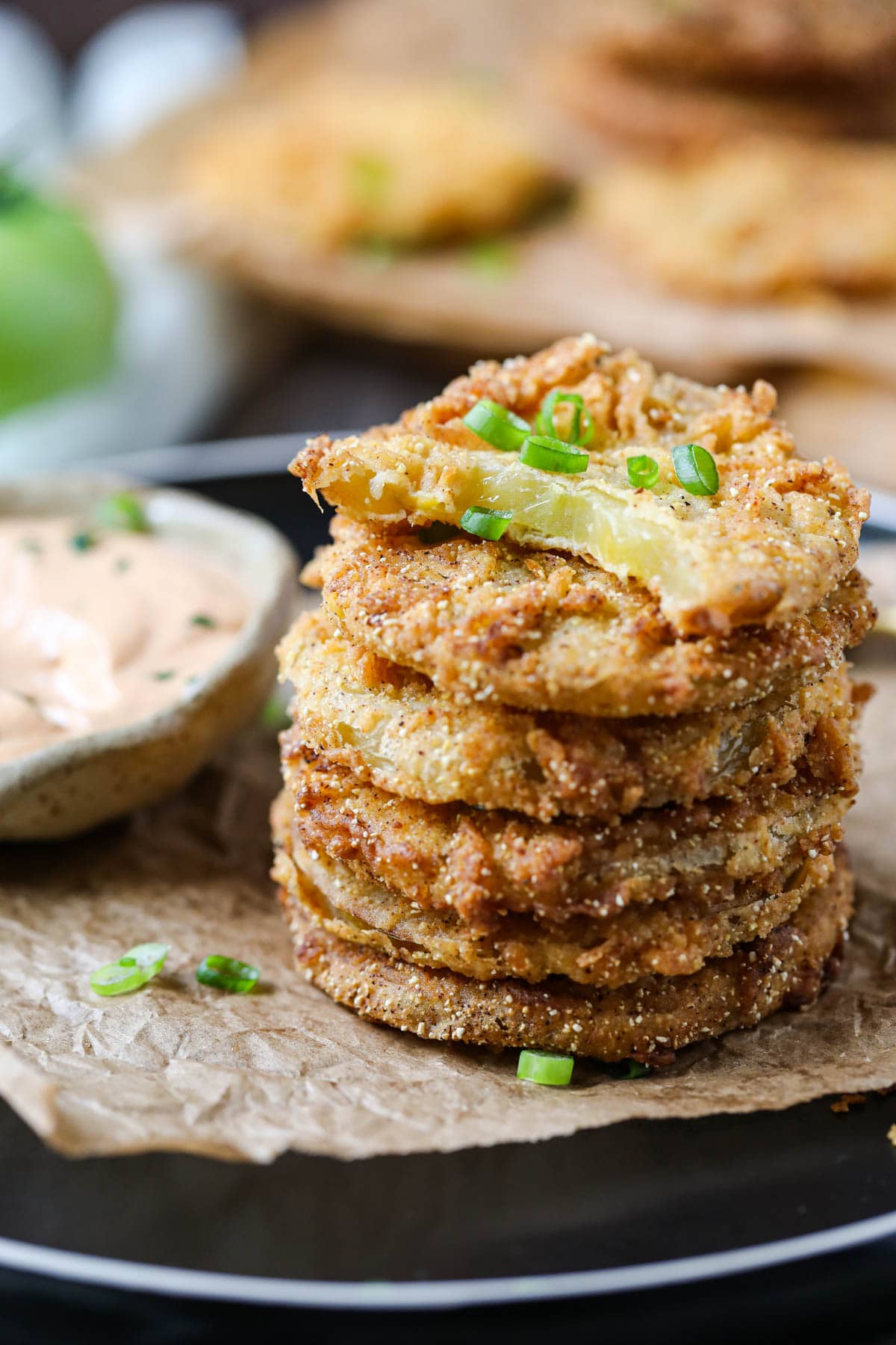 fried green tomatoes stacked on a black plate served with creamy dipping sauce in a cup.