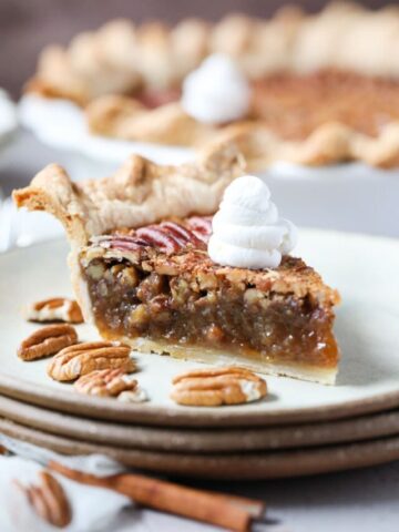 slice of southern pecan pie topped with whipped cream on a gray plate with whole pie in the background.
