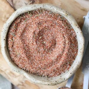 cajun seasoning in a brown bowl on a wooden cutting board.