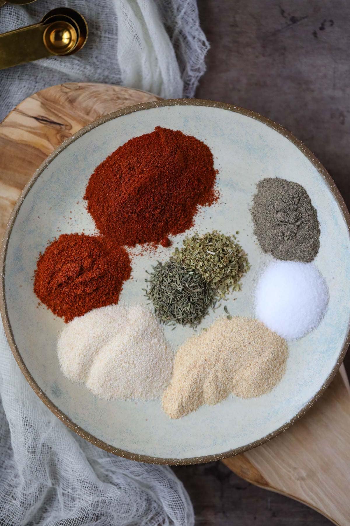 cajun seasoning ingredients on a gray plate on a wooden cutting board.