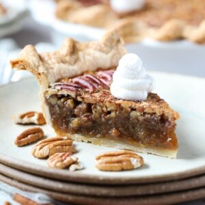 slice of southern pecan pie topped with whipped cream on a gray plate with whole pie in the background.