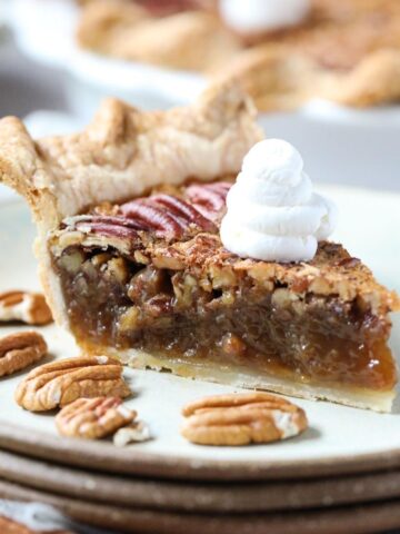 slice of southern pecan pie topped with whipped cream on a gray plate with whole pie in the background.