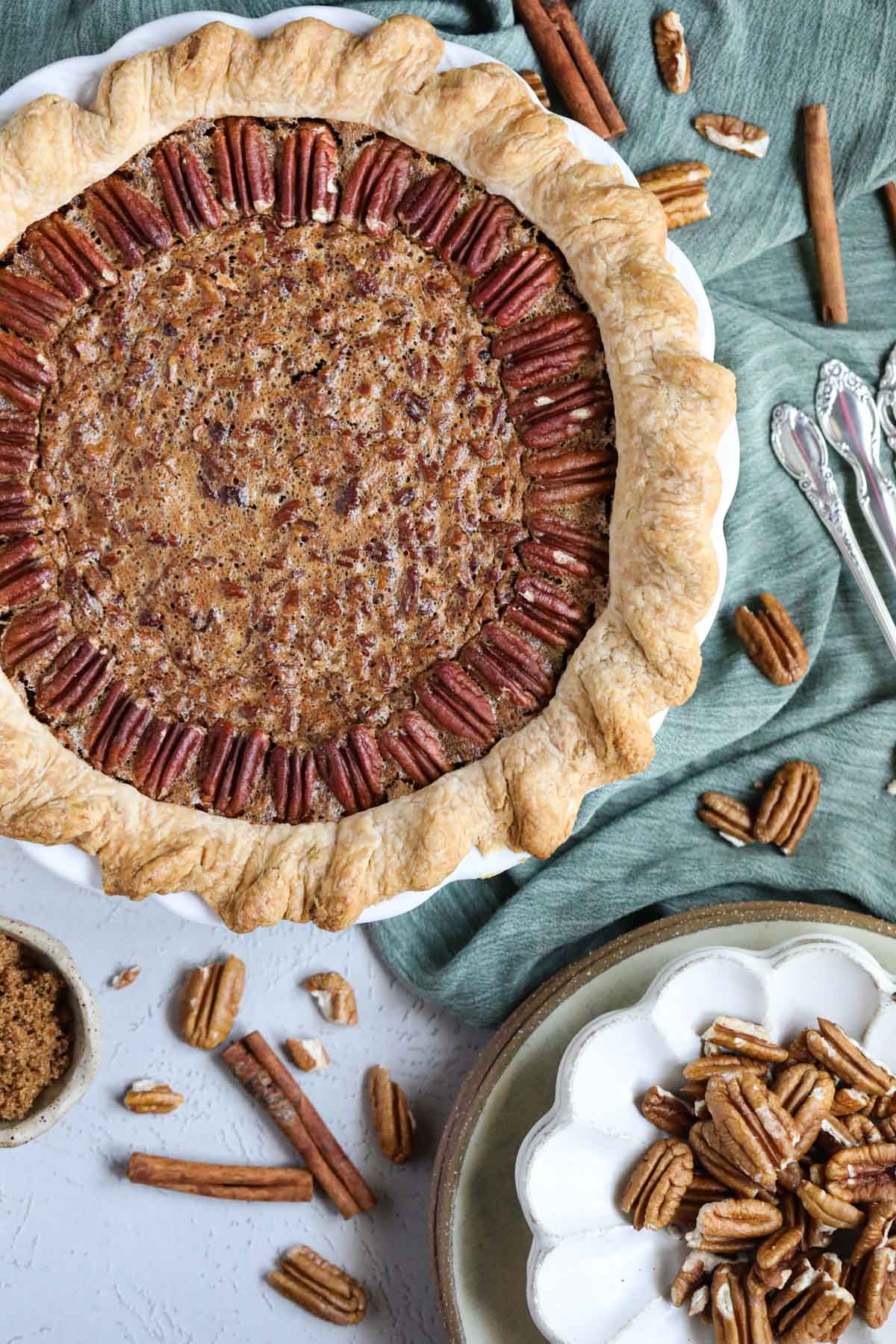 southern pecan pie with a green linen underneath on a white surface with a bowl of pecans in the bottom corner.