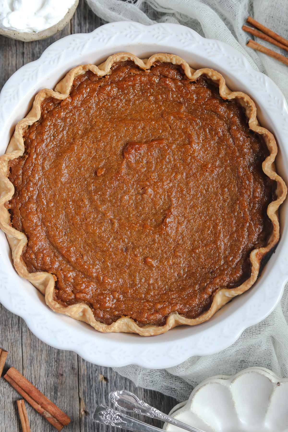 southern sweet potato pie in a white pie dish on a wooden table.