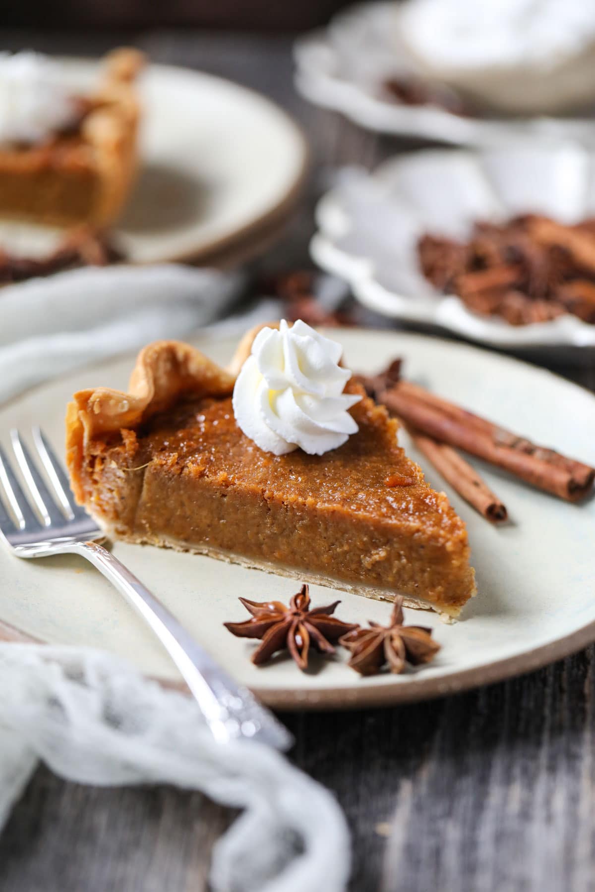 slice of southern sweet potato pie on a gray plate with whipped cream on top and silver fork on plate.