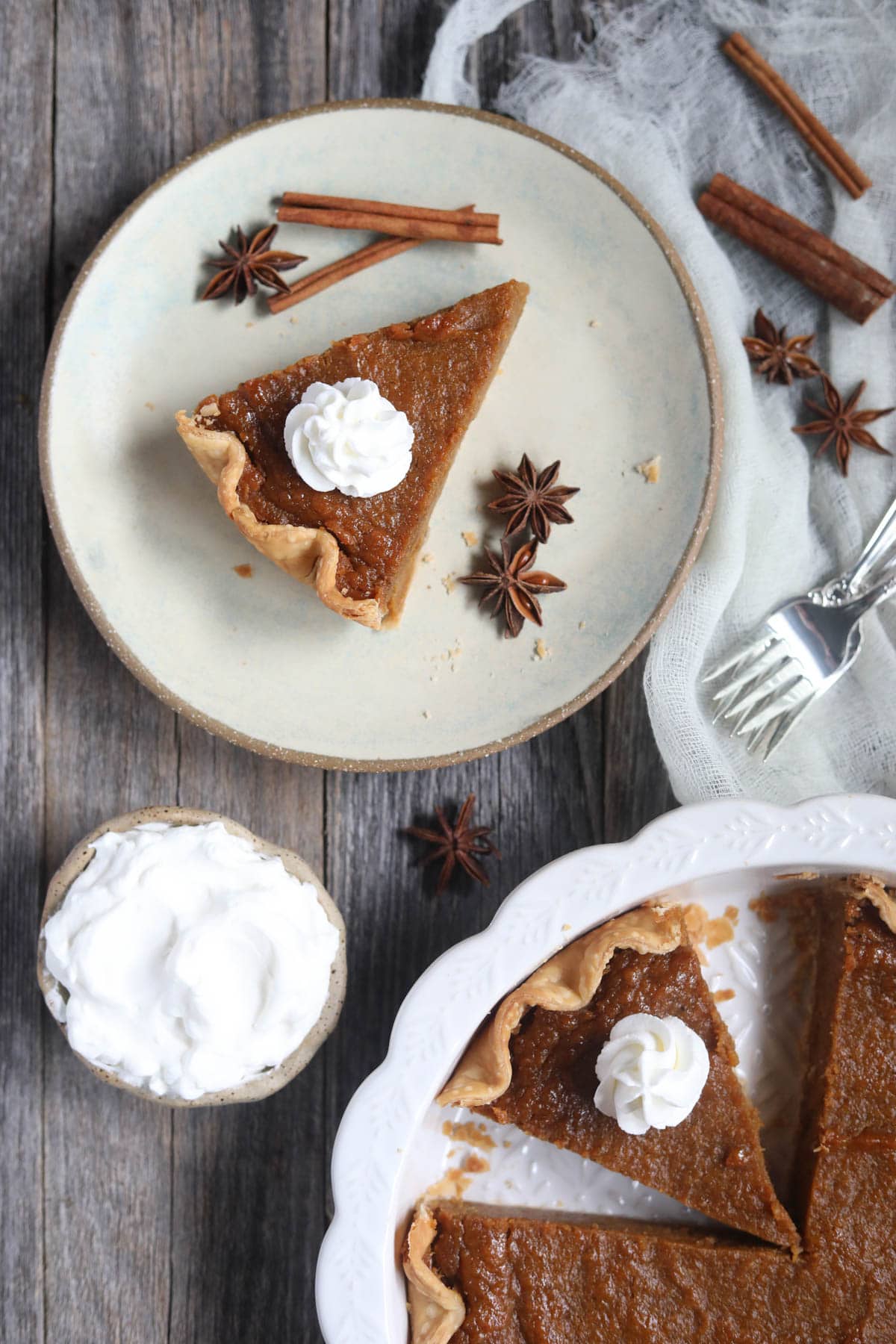 southern sweet potato pie sliced in a white pie dish and a single slice on a plate with whipped cream on a wooden surface.