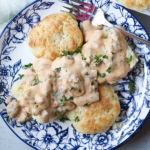 biscuits and gravy on a blue and white plate with a pan of biscuits in the top right corner.