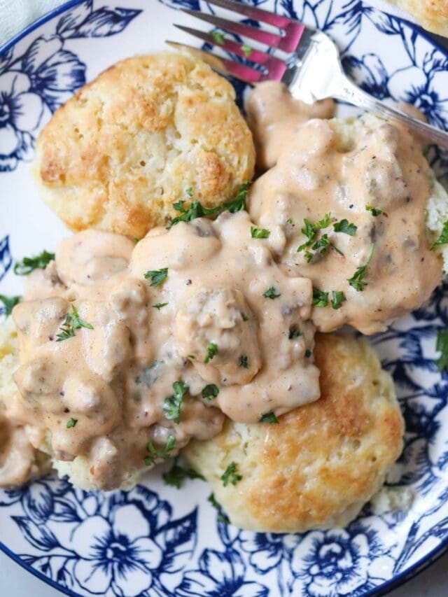 biscuits and gravy on a blue and white plate with a pan of biscuits in the top right corner.