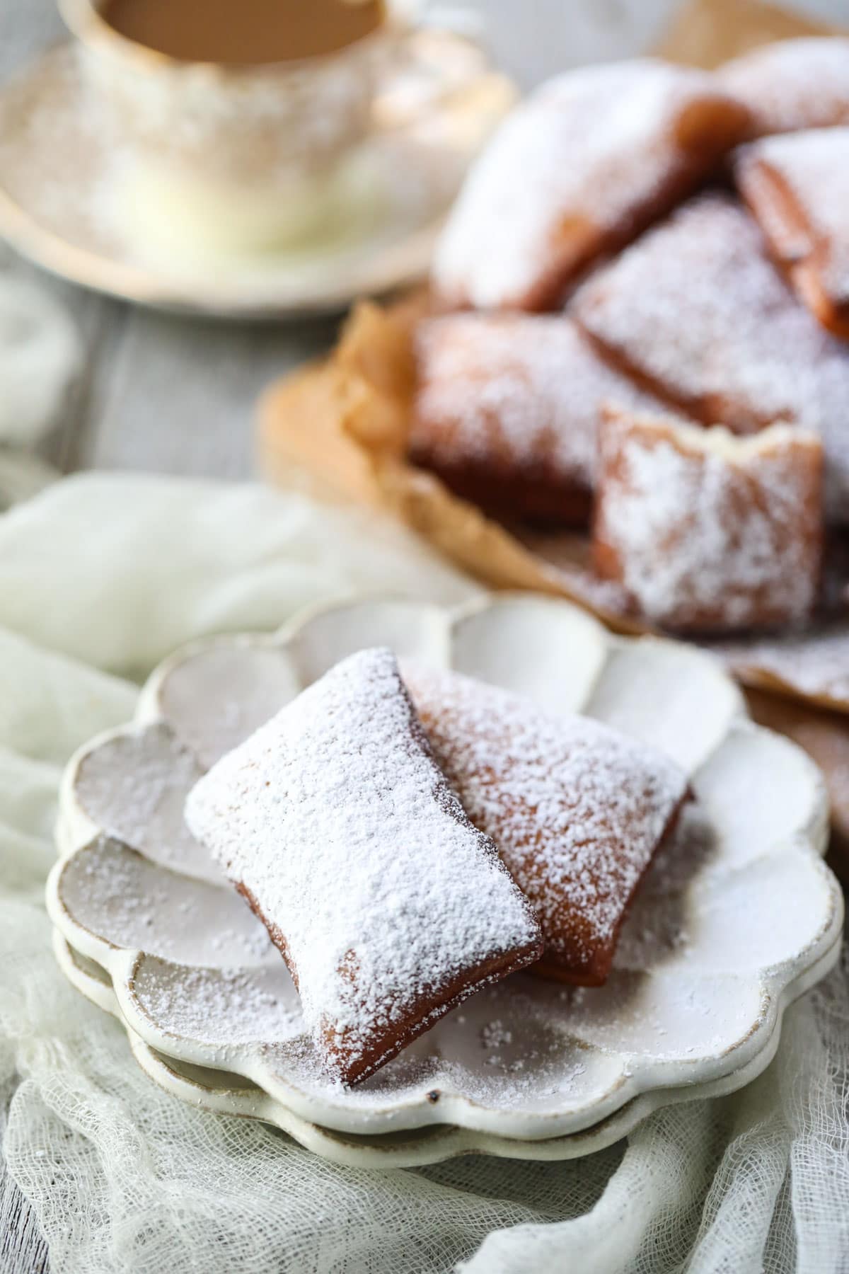 beignets on a white plate with a cup of coffee in the background.