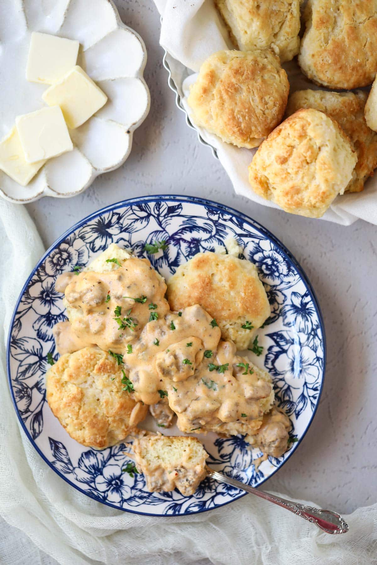 biscuits and gravy on a blue and white plate with a pan of biscuits in the top right corner.