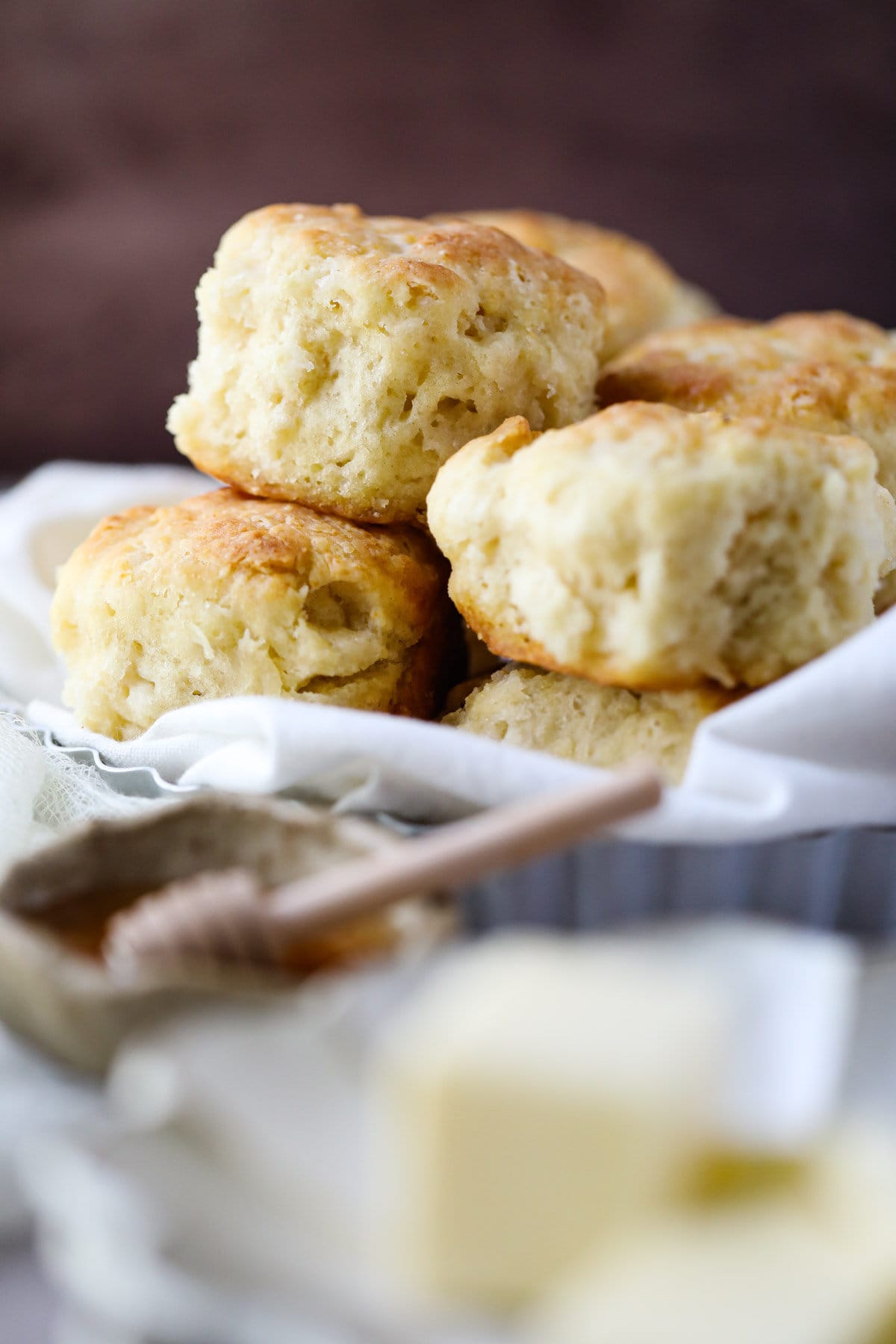 homemade buttermilk biscuits stacked in a pan with honey and butter in the front of the shot.