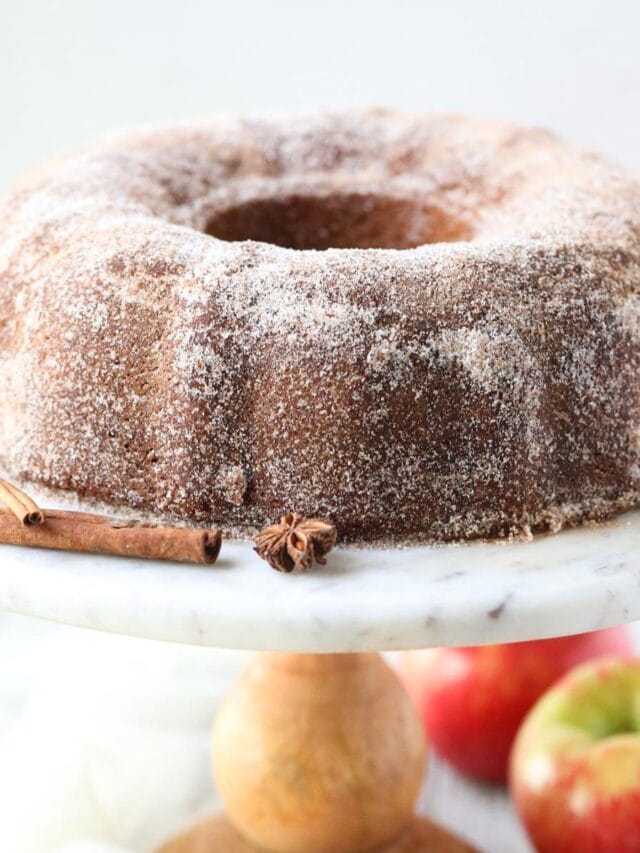 apple cider donut cake on a wooden cake stand.