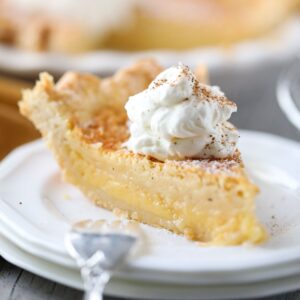 buttermilk pie slice on a white plate with whole pie in the background.