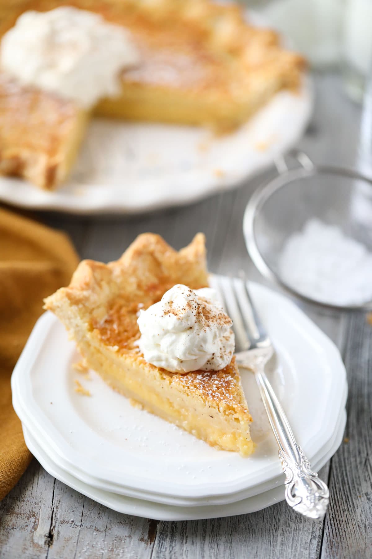 buttermilk pie slice on a white plate with whole pie in the background.