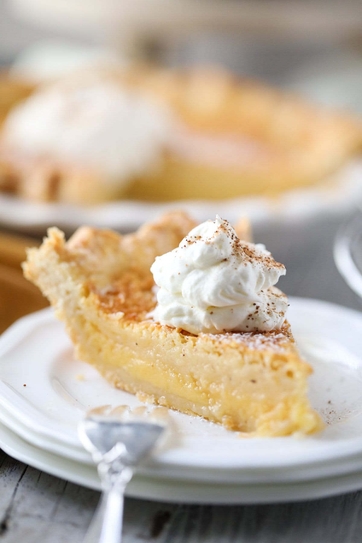 buttermilk pie slice on a white plate with whole pie in the background.