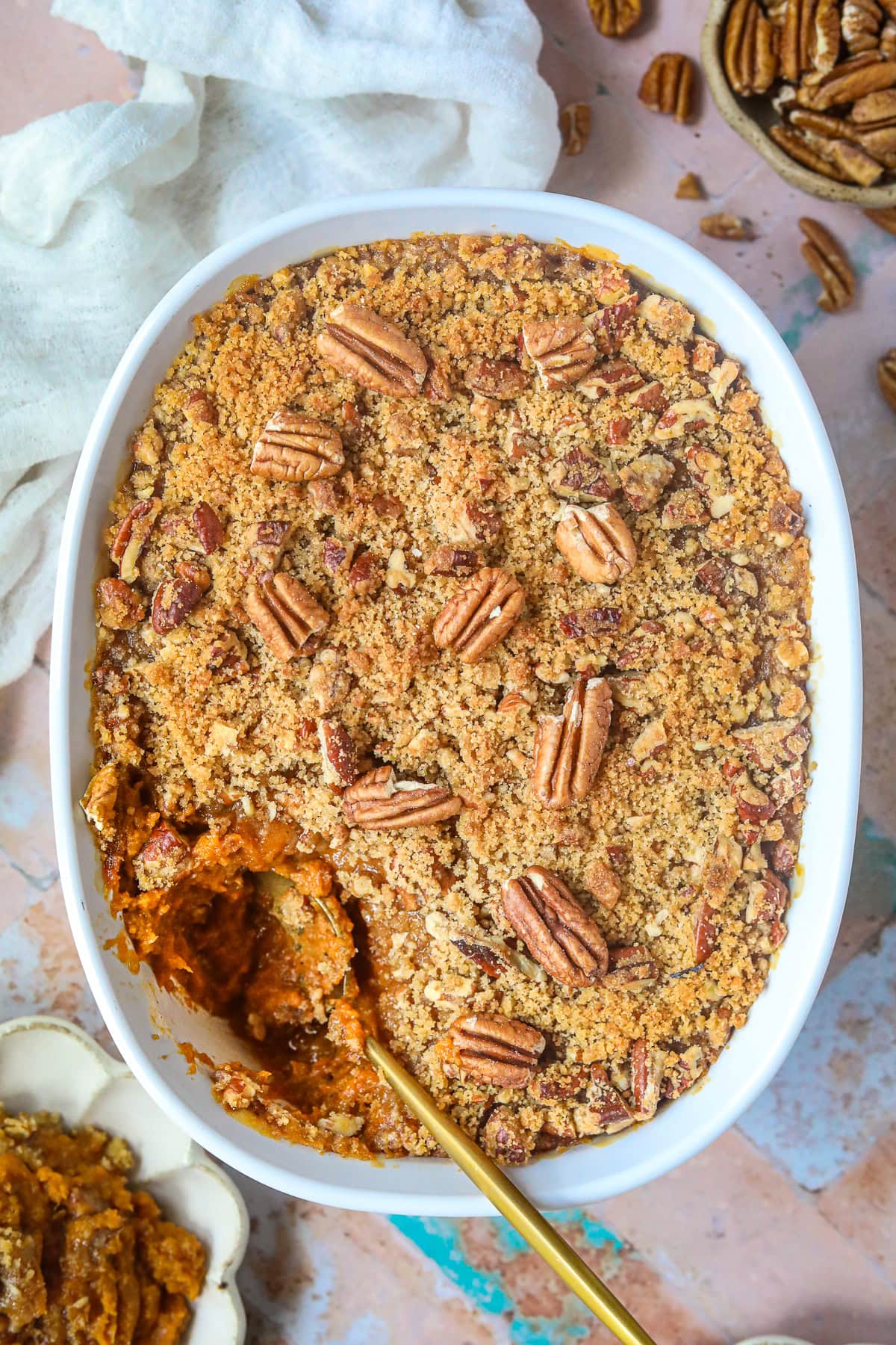 Sweet potato casserole with pecans and crumble topping in a baking dish on a table top.