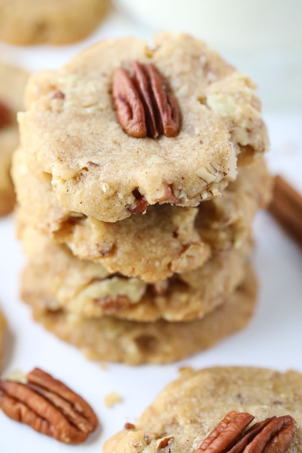 pecan sandies stacked on a white table with pecan halves scattered around.