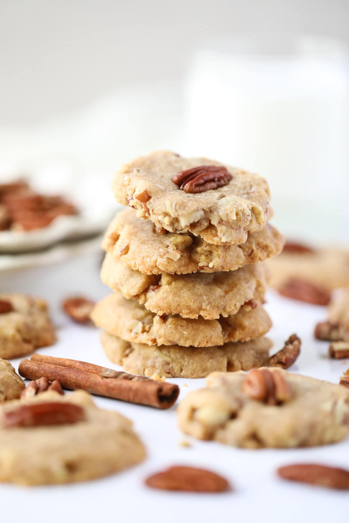 pecan sandies stacked on a white table with pecan halves scattered around.