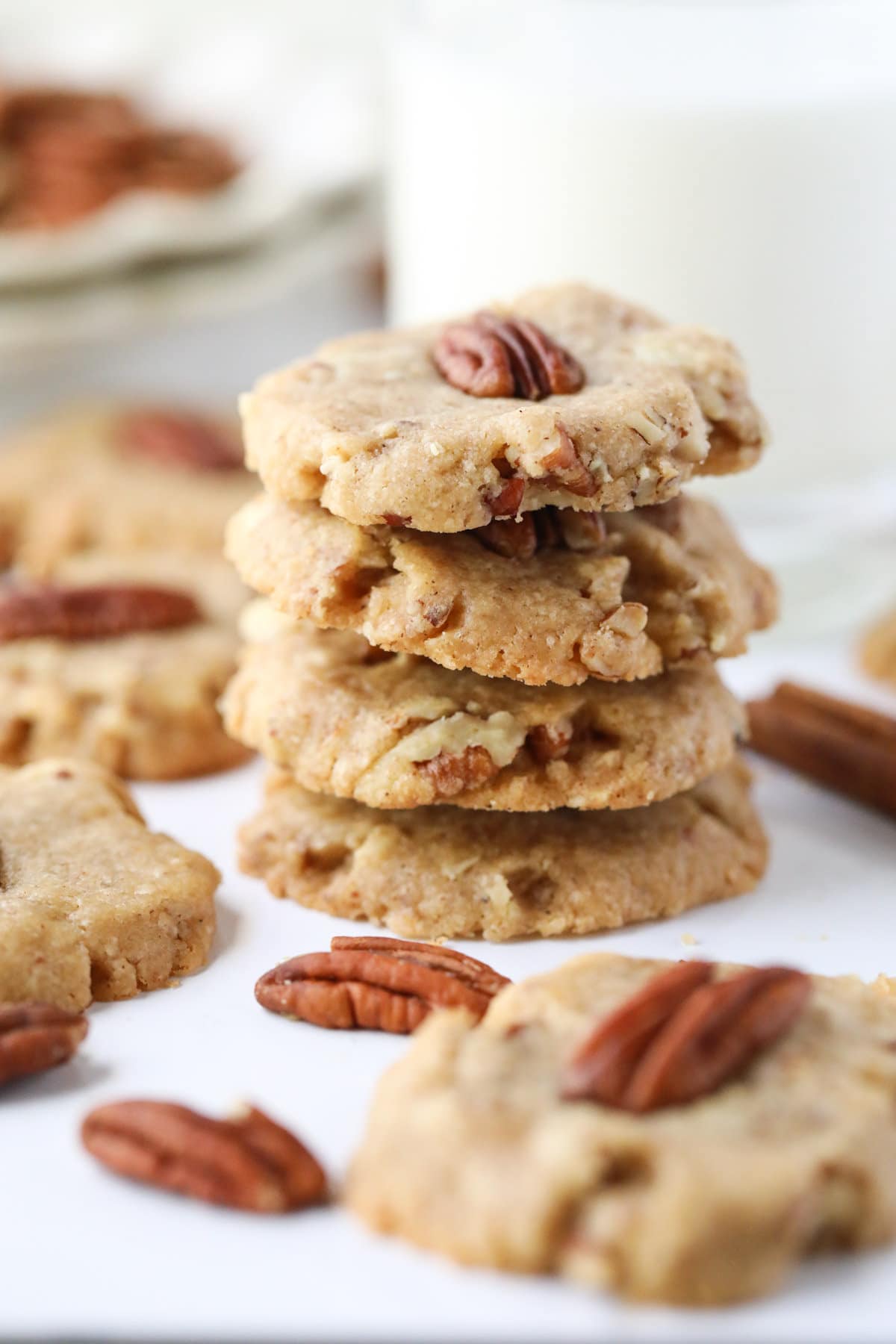 pecan sandies stacked on a white table with pecan halves scattered around.